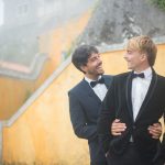 A joyful gay couple in tuxedos sharing a romantic moment outdoors in Portugal.